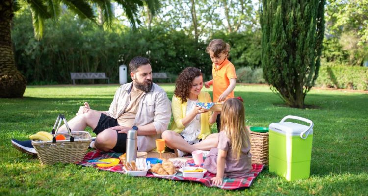 A family having a joyful picnic in a sunny park with fresh food and drinks.