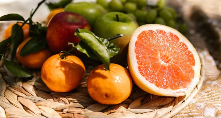 Vibrant assortment of fresh fruit including citrus and apples placed in a natural setting.